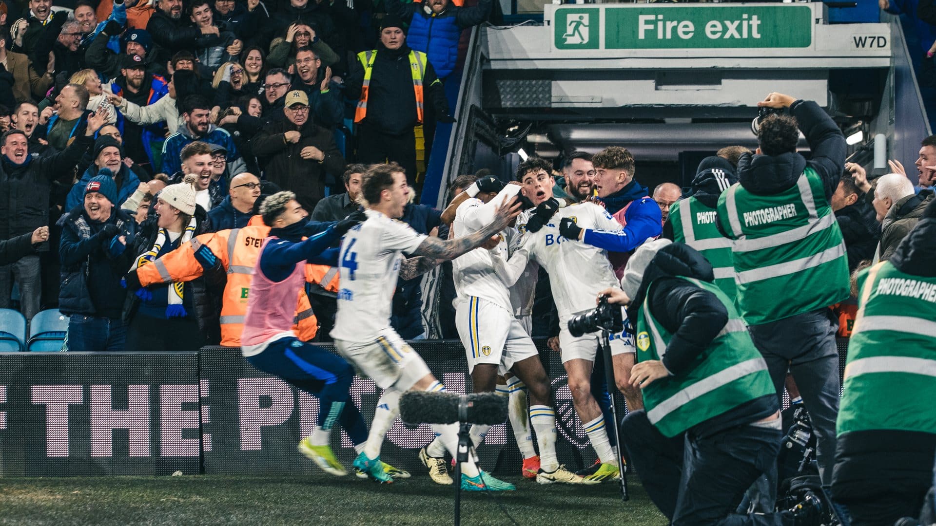 Archie Gray getting pulled around by Charlie Cresswell, as to the left Leeds players run in to celebrate with him, and to the right green-jacketed photographers run to the scene