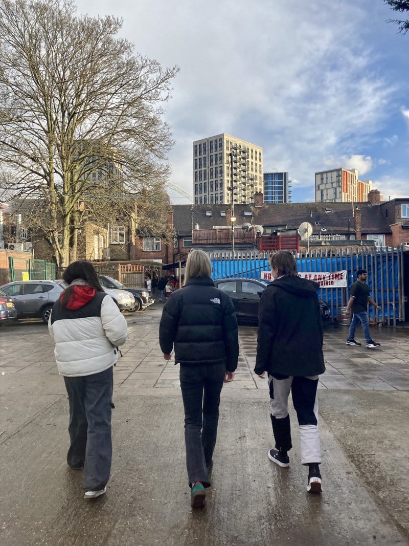 A photo from the hunt for a Guinness vs first home mortgage battleground in London, three of us walking between steel gates and terraced houses while tower blocks loom on the horizon