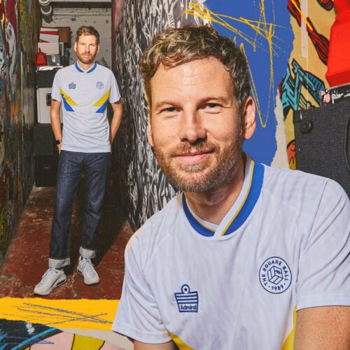Two photos of Simon Rix from Kaiser Chiefs wearing our TSB x Admiral collab football shirt, which is white with a blue v-neck collar, blue and yellow chest flashes, and the TSB and Admiral logos on the chest