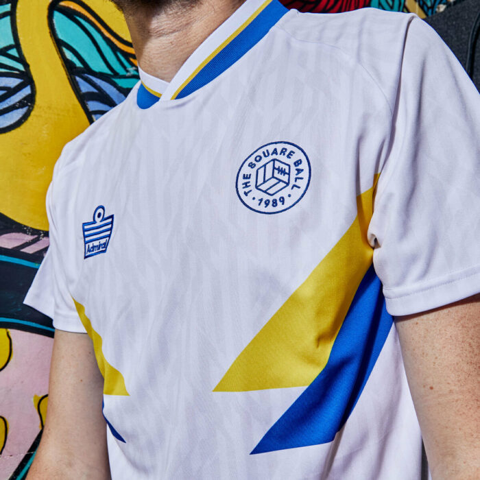 Simon Rix from Kaiser Chiefs wearing our TSB x Admiral collab football shirt, which is white with a blue v-neck collar, blue and yellow chest flashes, and the TSB and Admiral logos on the chest