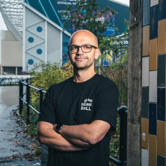 A photo of Michael wearing our retro logo t-shirt, showing a backprint featuring logos and graphics from throughout our history, and a front pocket print of the logo from the very first issue.