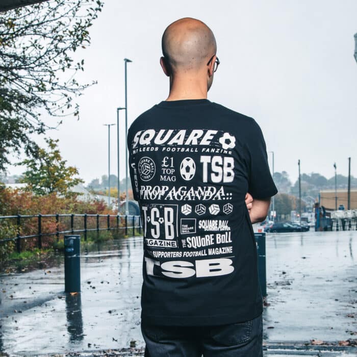 A photo of Michael wearing our retro logo t-shirt, showing a backprint featuring logos and graphics from throughout our history, and a front pocket print of the logo from the very first issue.