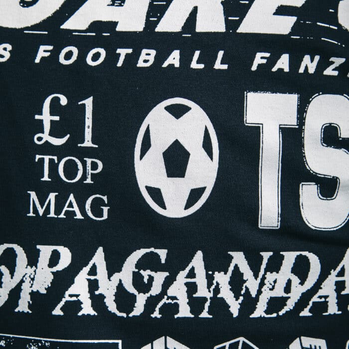 A close up photo of our retro logo t-shirt, showing a backprint featuring logos and graphics from throughout our history, and a front pocket print of the logo from the very first issue.