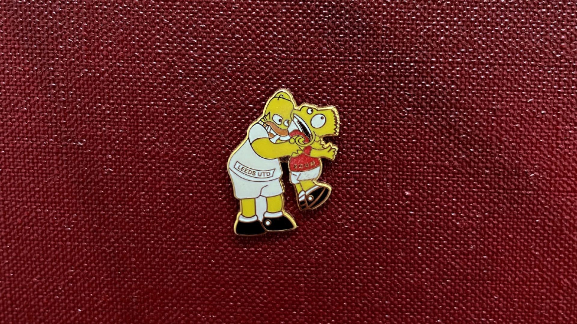 A pin badge of Homer Simpson in a Leeds shirt strangling Bart in a Scum kit