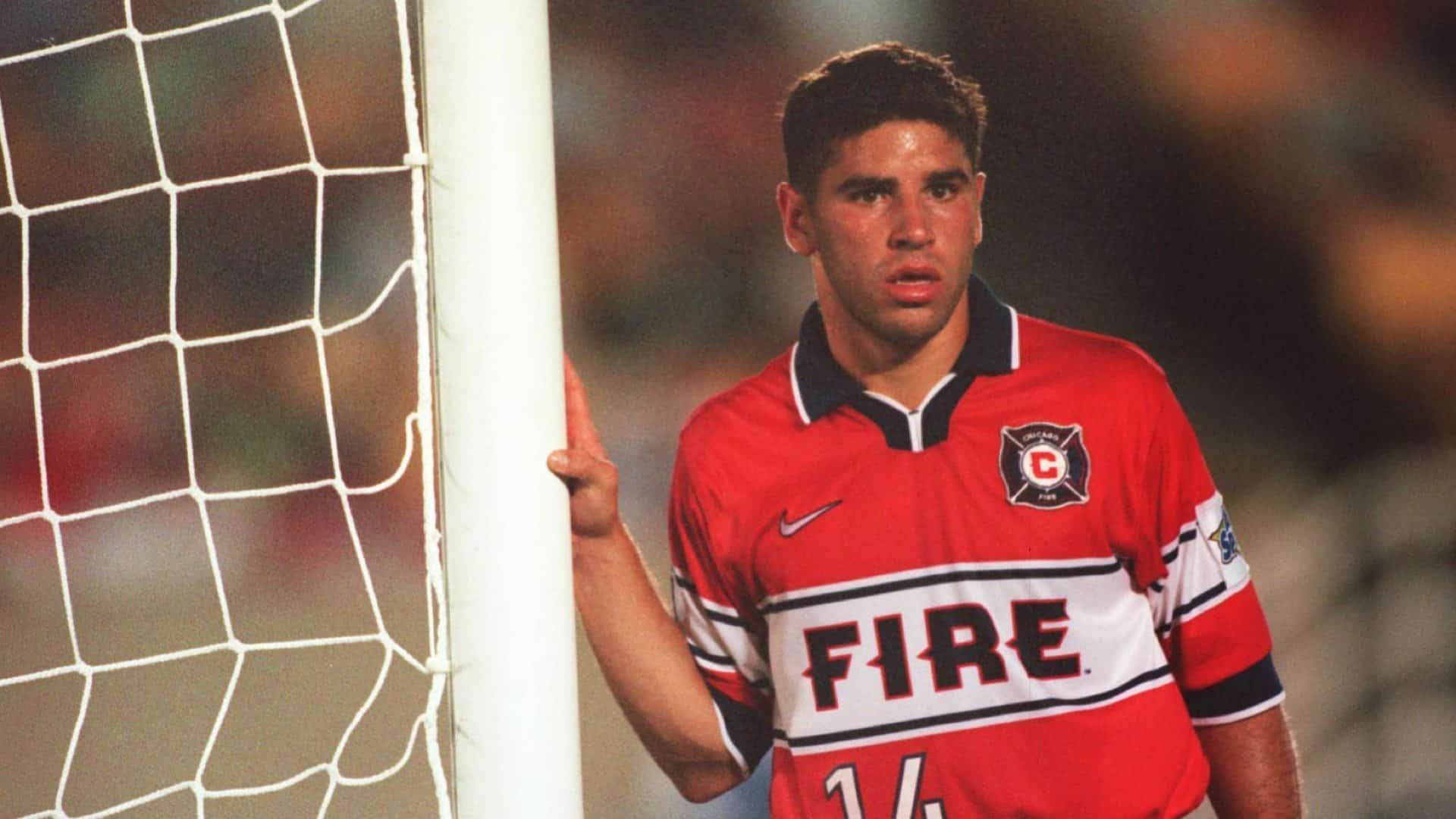 Chris Armas, Leeds' new assistant coach, leaning against a goalpost while playing for Chicago Fire against Dallas Burn in 1999. He's wearing a really cool dark orange jersey with 'FIRE' written across it in a white band