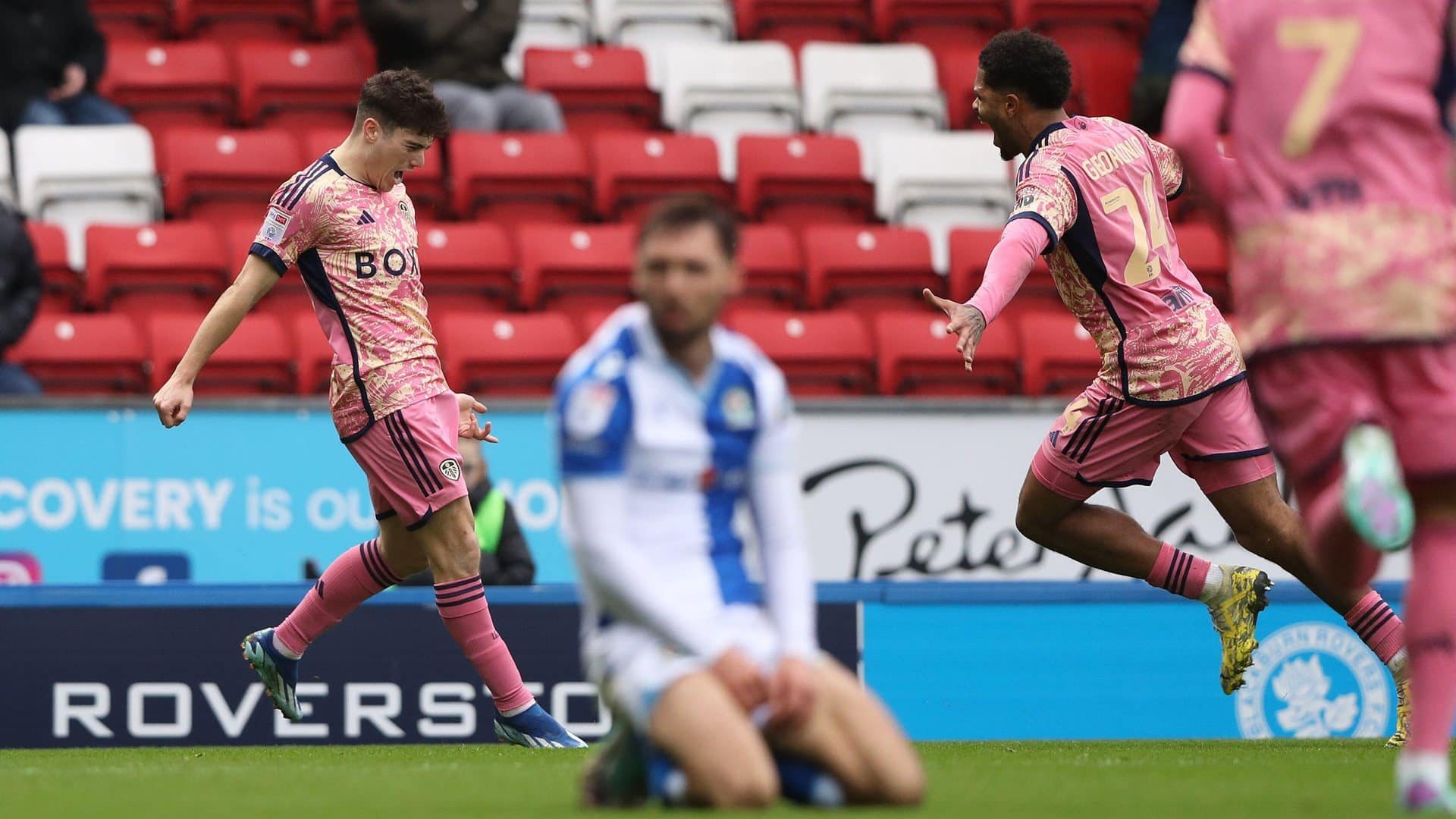 Dan James with his arms down wrists back celebration as Rutter runs to greet him and a Blackburn player slumps to his knees in the blurry foreground