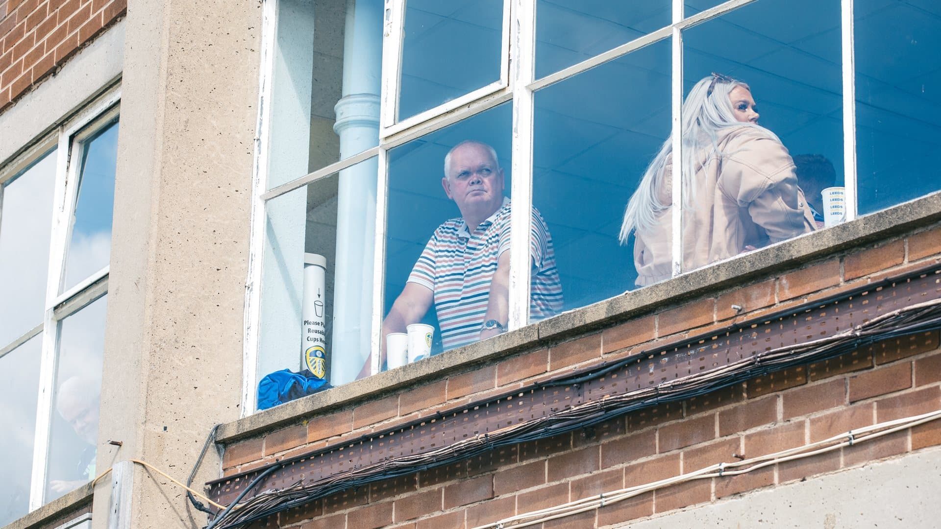 Two Leeds fans in one of the NW corner bars, viewed through the window from outside Elland Road stadium, one of them leaning on the windowledge and gazing out at Beeston