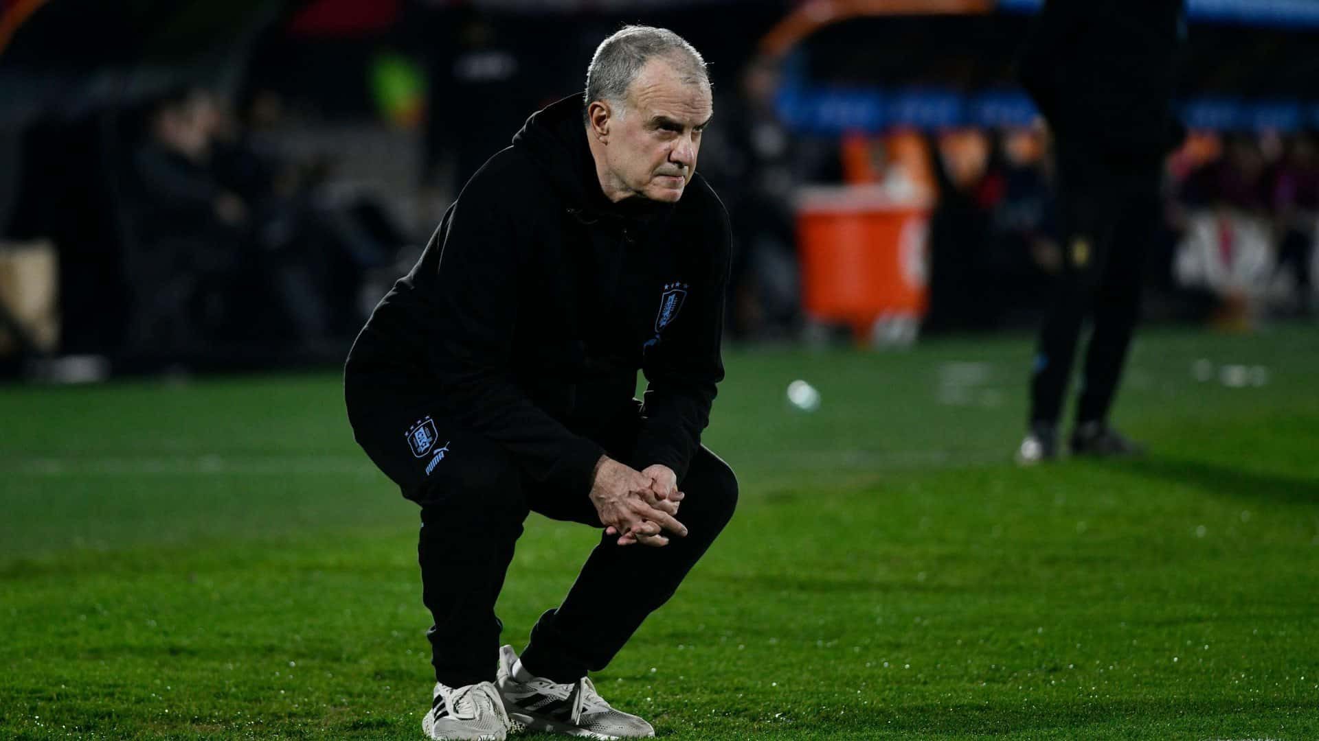 Marcelo Bielsa, in all black with white trainers, crouching on the touchline in typical style during Uruguay vs Chile. Those hamstrings!