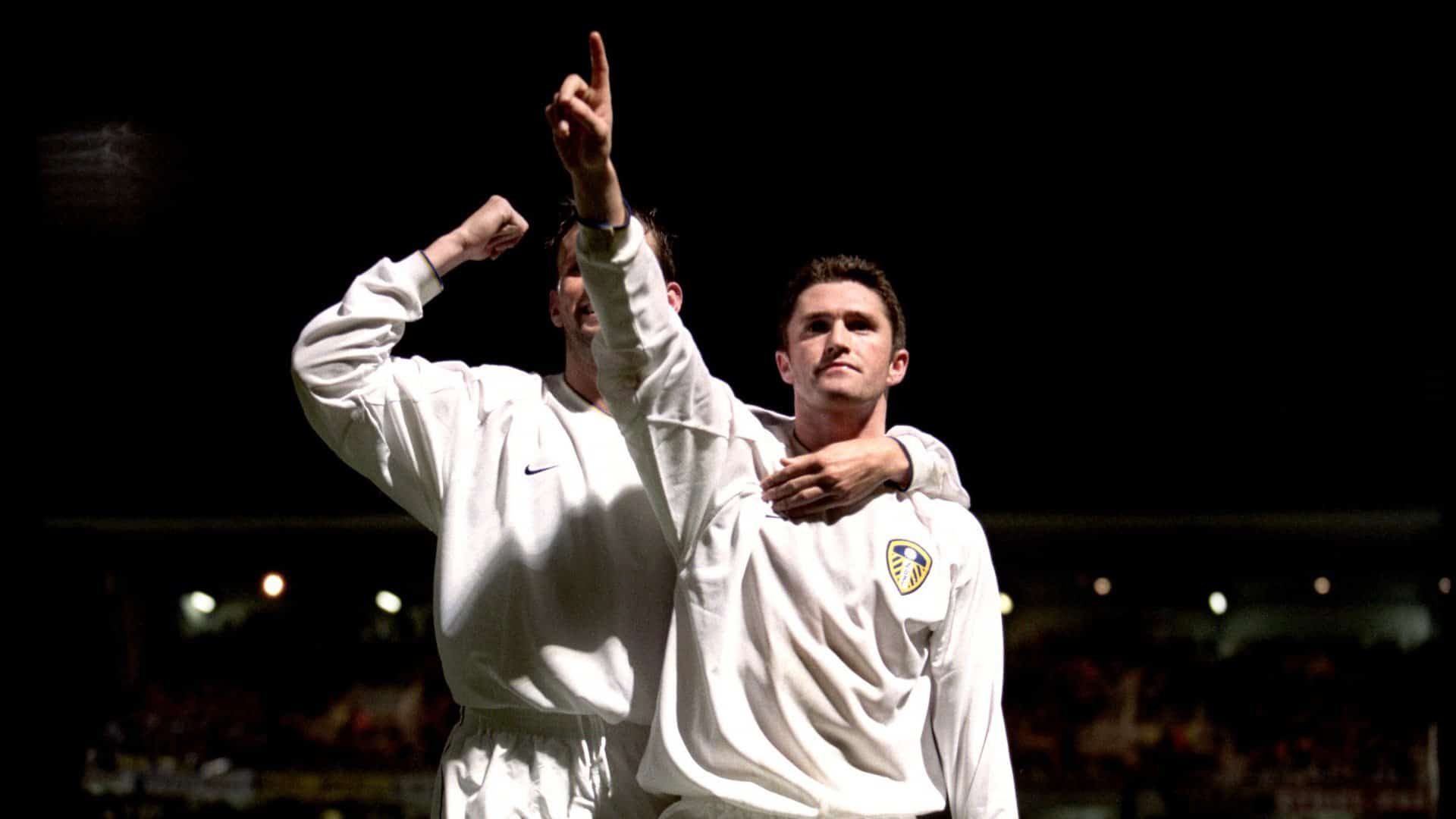 Robbie Keane celebrating his goal for Leeds against Troyes by raising his finger in the air and taking a hug of Eirik Bakke. Unusually, his all-white Nike Leeds shirt is sponsorless, because of the French ban on alcohol advertising meaning no Strongbow allowed