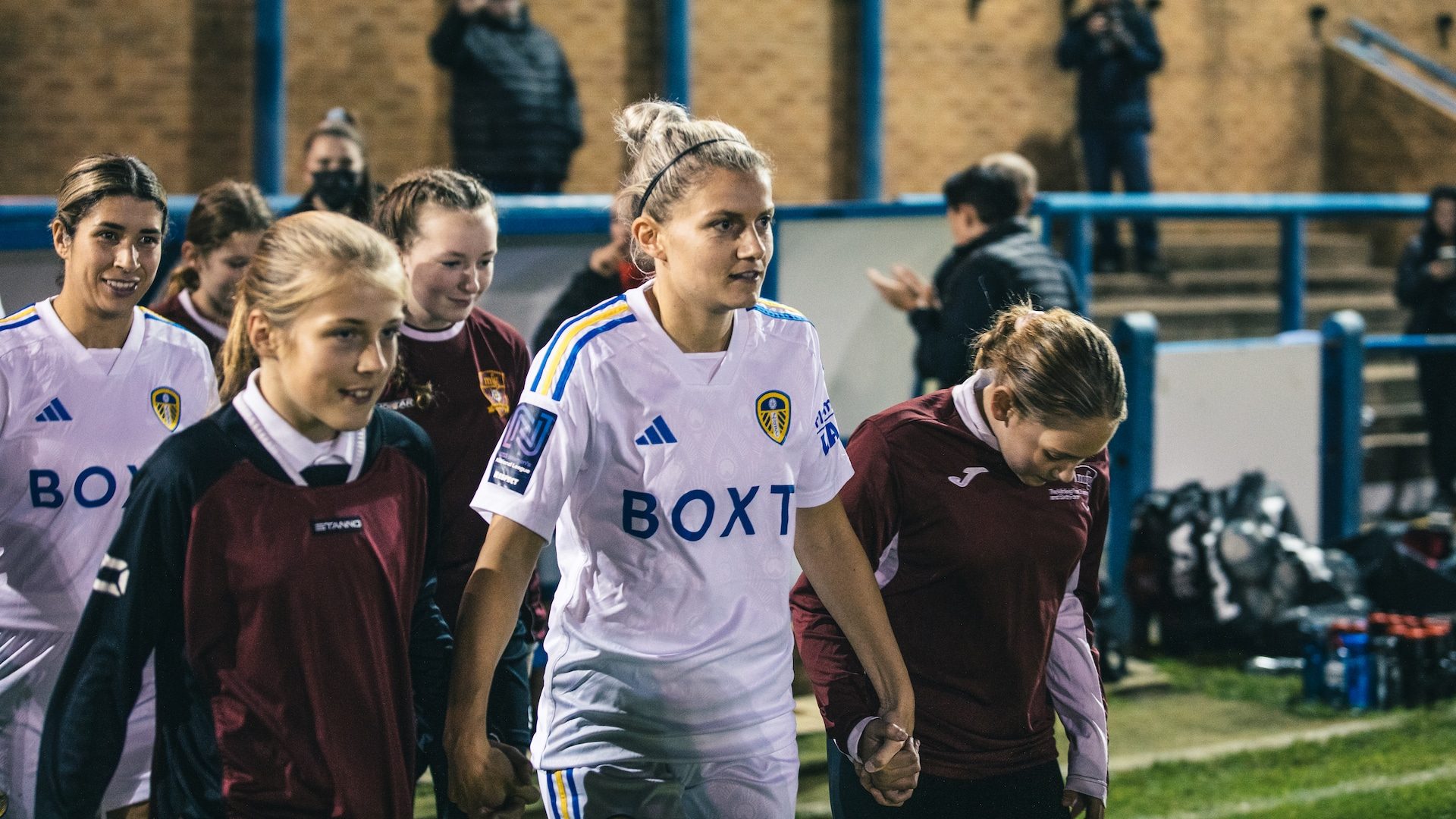 A photograph of Sarah Danby walking out of the tunnel for Leeds United Women with two mascots either side of her