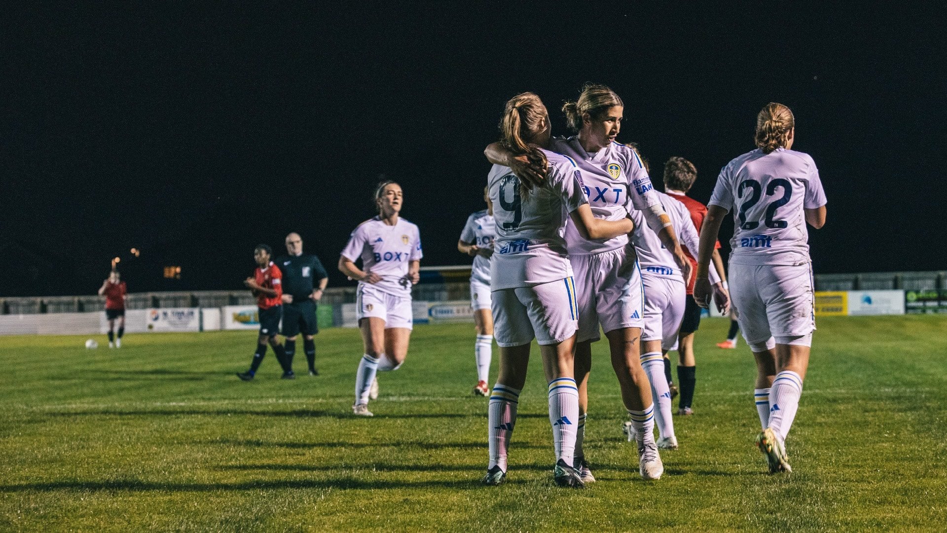 Leeds United Women players celebrating under the floodlights against FCUM