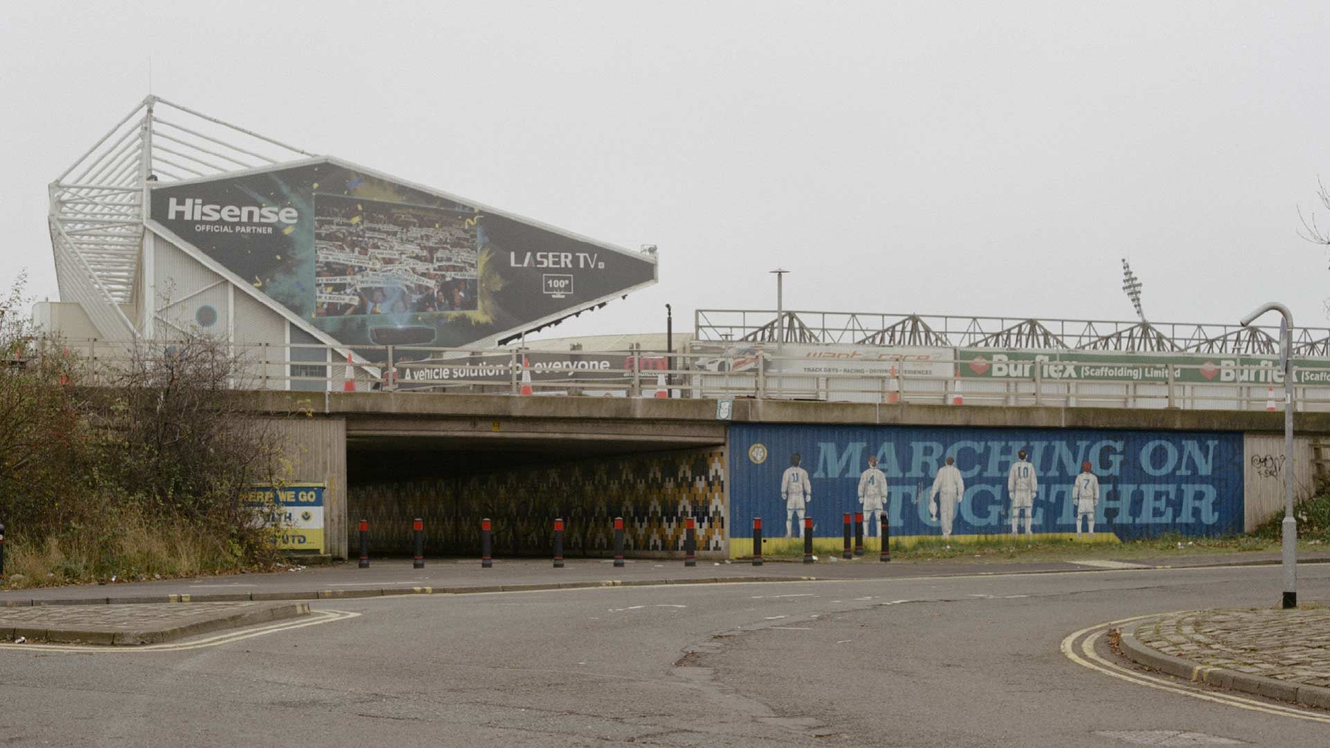 A cool photograph by Kate Schultze of the mural next to the Lowfields tunnel with the East Stand of Elland Road it the background. Everything is grey