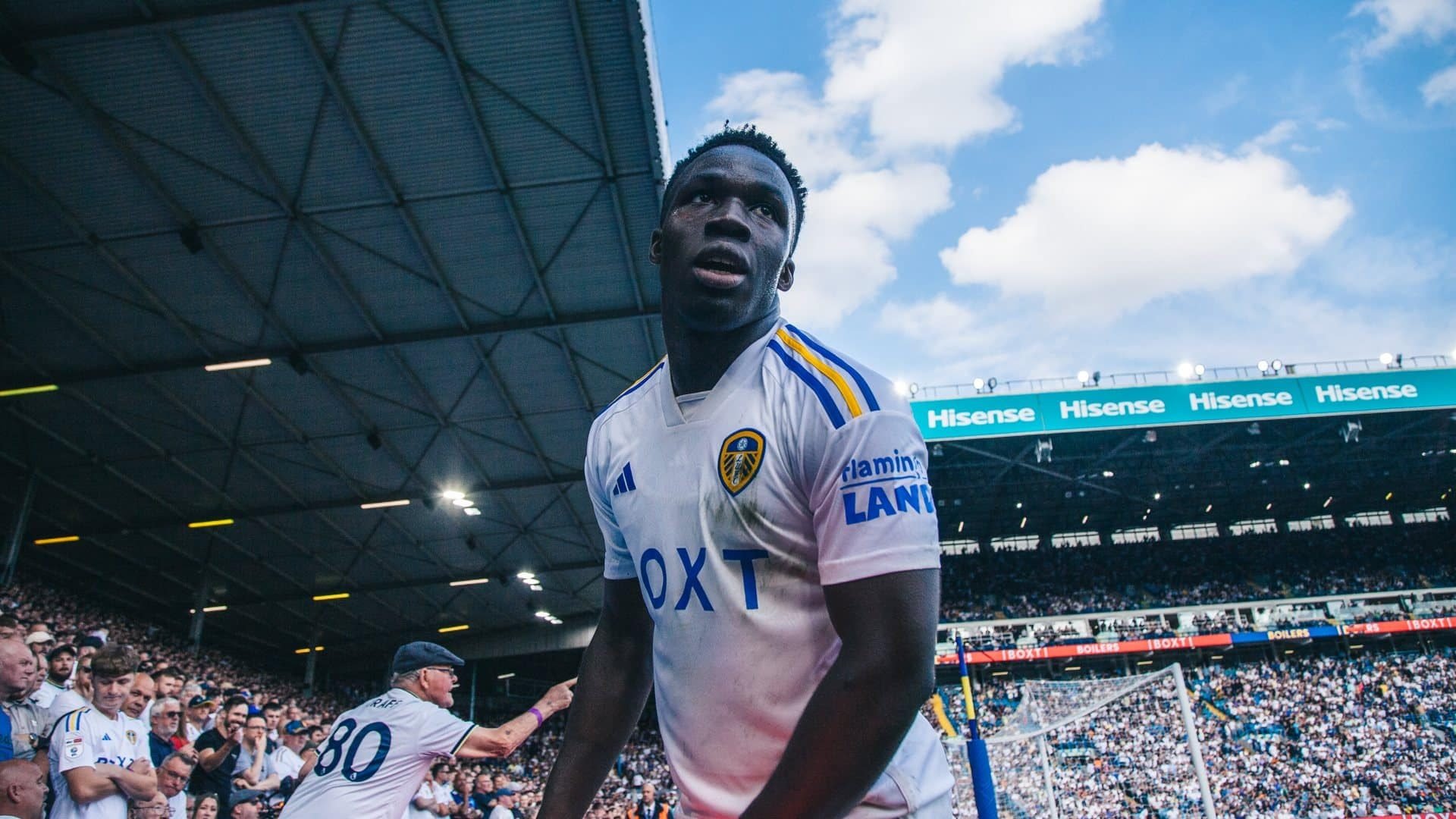 A close up photo of Wilf Gnonto in front of the Kop, viewed from below his chin. He's looking around as if wondering why he's not getting a penalty