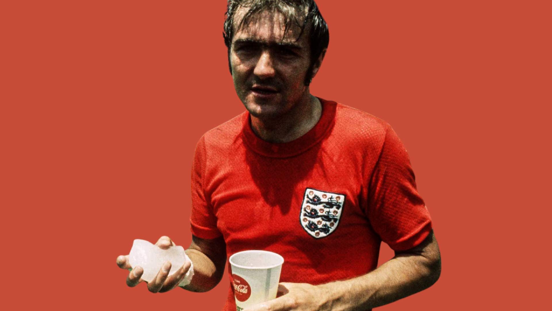 Terry Cooper, holding a block of ice in one hand and a paper Coca-Cola cup in the other, wearing England's red away kit at the 1970 World Cup, sweating a lot