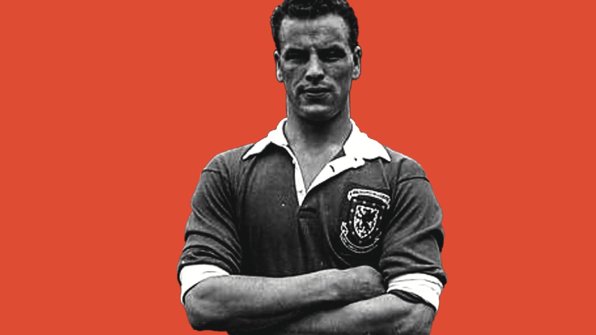 A black and white photo of John Charles with his arms folded in a Wales kit against a red backdrop