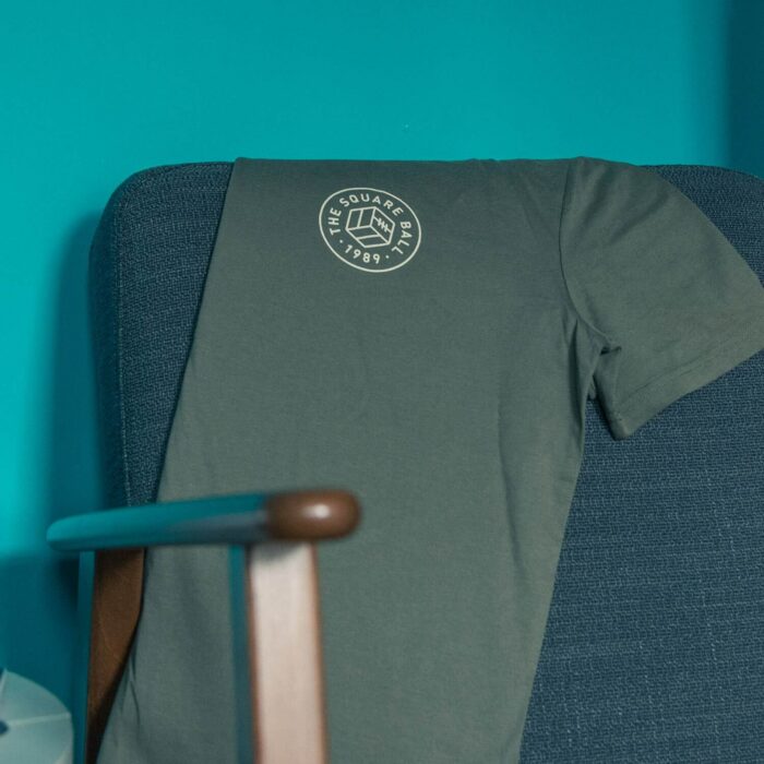 A khaki TSB pocket logo t-shirt draped on the back of a chair