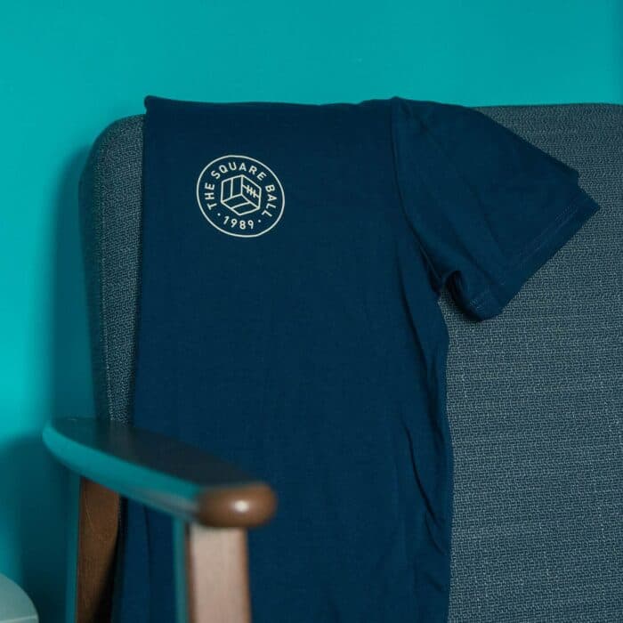 A navy TSB pocket logo t-shirt draped on the back of a chair